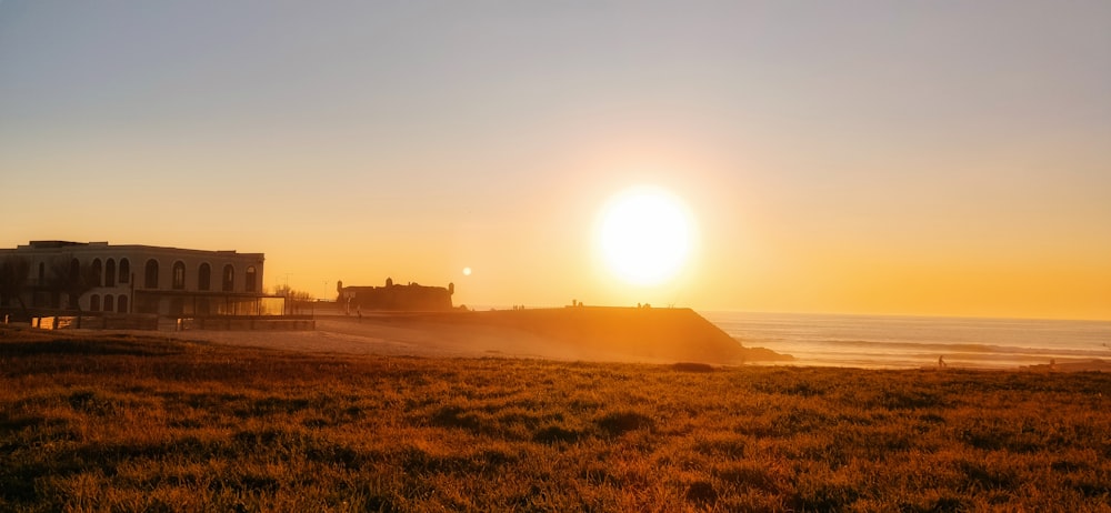 the sun is setting over a beach with a building in the background