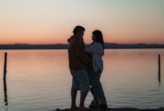 Couple sharing a quiet moment by a serene lake at sunset.