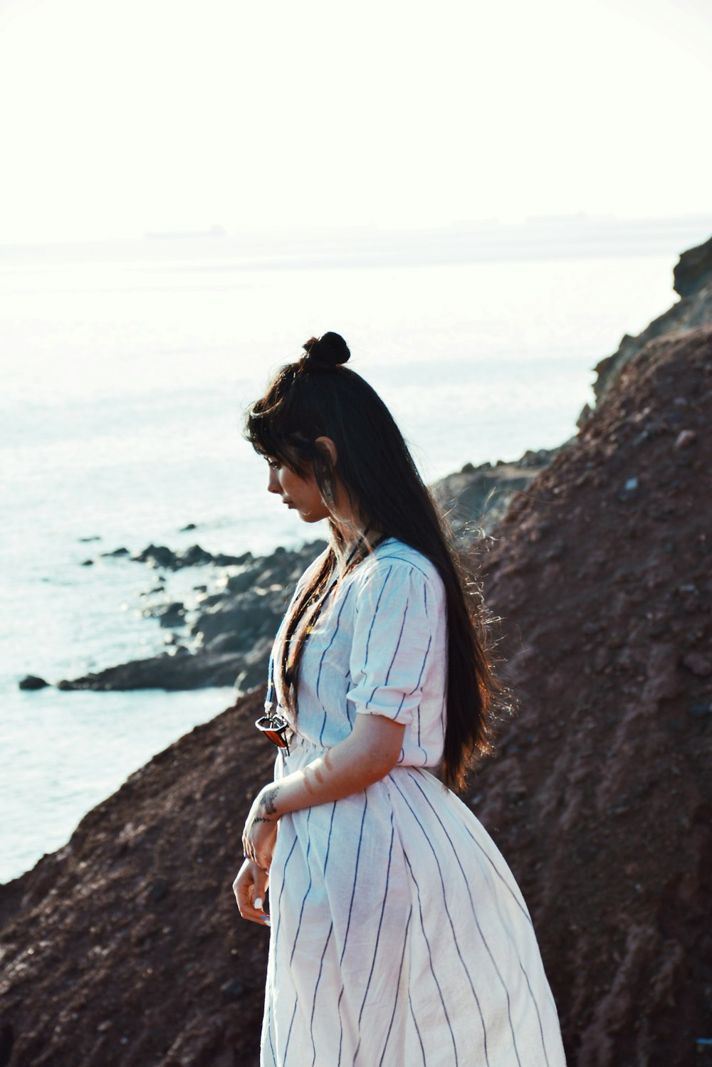 a woman in a white dress standing on a rocky beach