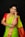 A woman in traditional attire, adorned with elaborate gold jewelry and a vibrant saree. Her hair is neatly styled and she has henna designs on her hand. The saree features a combination of green and red colors with intricate patterns.