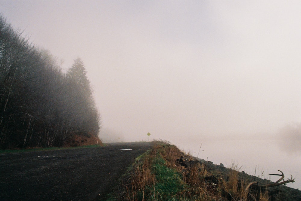 a foggy road next to a body of water