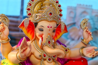 A colorful, intricately designed statue of a deity with an elephant head adorned with numerous gems and ornaments. The statue is holding objects in multiple hands, and the craftsmanship features vibrant colors and elaborate detailing.