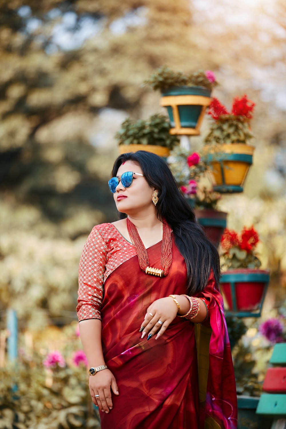 a woman in a red sari standing in front of potted plants