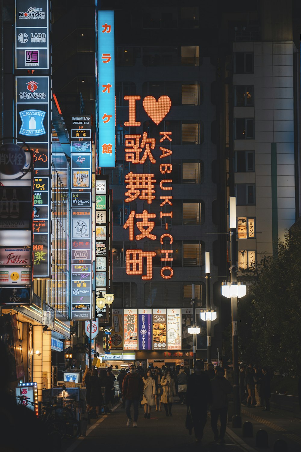 a city street at night with people walking on the sidewalk