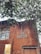 A brick building with a sign reading 'ZEBA DESIGN CENTRE'. Part of the building’s facade includes large windows and a smaller section with a lit interior visible through a glass panel. Above the building, tree branches with green leaves extend across the upper part of the image.