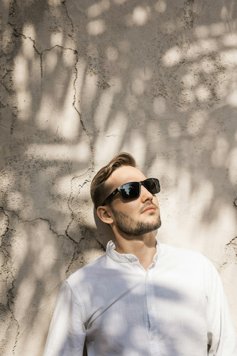 a man wearing sunglasses standing in front of a wall