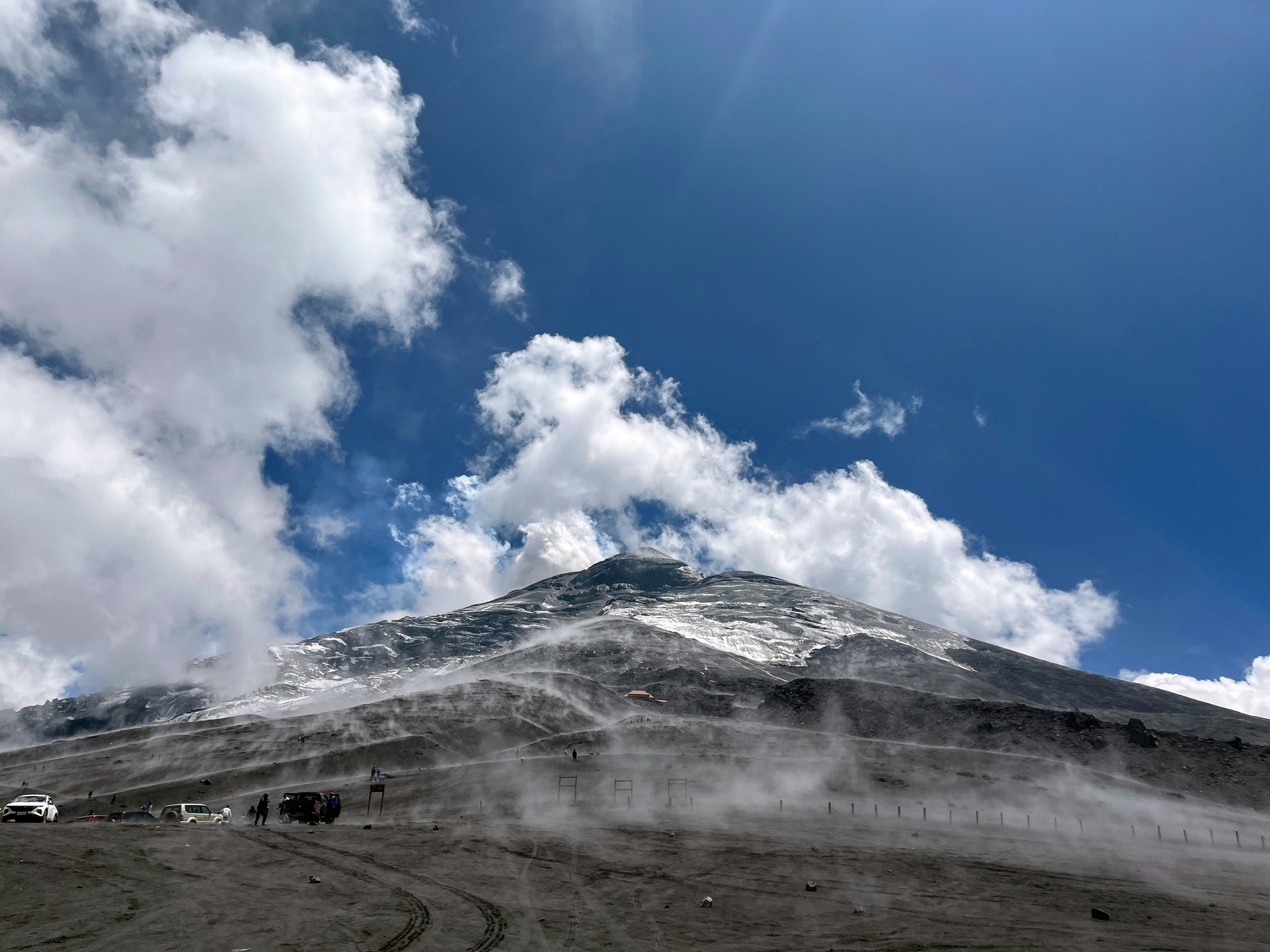 a mountain covered in snow under a partly cloudy sky, Ash on Cotopaxi volcano