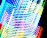 An array of brightly colored vertical lines, possibly created using long exposure photography. The colors blend and overlap, creating a dynamic and vibrant composition.