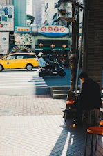 A motorcycle taxi driver using the Motopulse app on a smartphone while waiting at a busy city street corner.