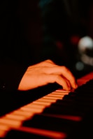 Close-up of a hand gently touching a piano keyboard under warm ambient lighting.