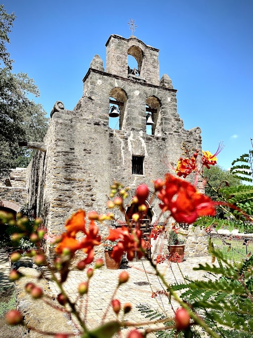 a stone building with a bell tower and flowers in the foreground