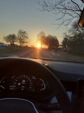 A close-up of hands on a steering wheel with a scenic road ahead at sunset.