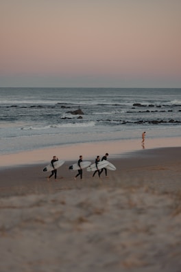 Group of friends laughing on the beach with surfboards in hand.