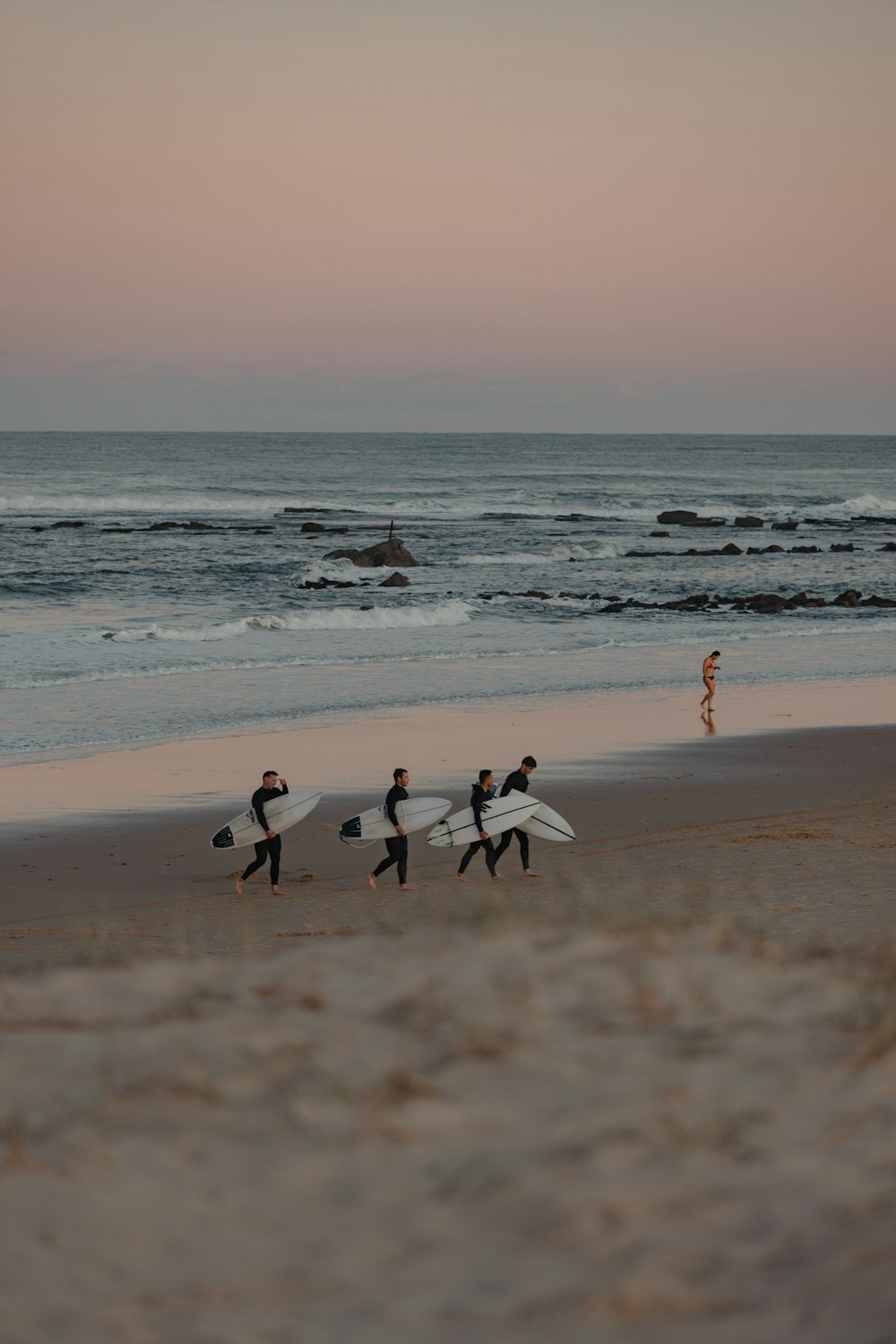 a group of people walking along a beach holding surfboards
