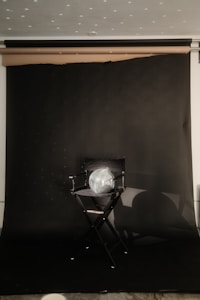 A director's chair is placed against a dark backdrop with a reflective disco ball resting on the seat. Light reflects off the disco ball, creating scattered spots of light on the backdrop. The setting appears to be a studio or a staged area for photography or film.