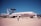 A military aircraft displayed on a runway, marked with 'U.S. AIR FORCE' on its fuselage. It has a large rotating radar dome on top and is surrounded by several people observing or walking by. The sky is clear and blue, and there are no clouds visible.