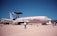 A military aircraft displayed on a runway, marked with 'U.S. AIR FORCE' on its fuselage. It has a large rotating radar dome on top and is surrounded by several people observing or walking by. The sky is clear and blue, and there are no clouds visible.