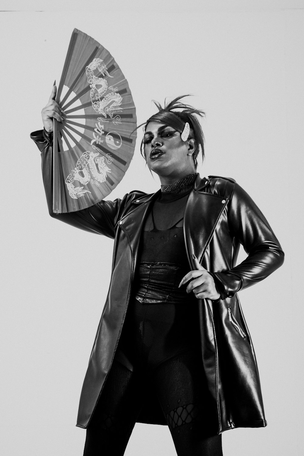 a woman in a leather coat holding a fan