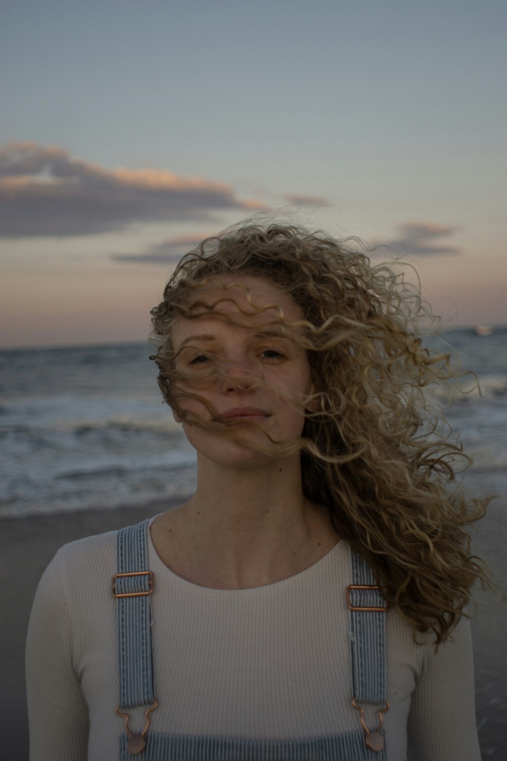 a woman standing on a beach with her hair blowing in the wind