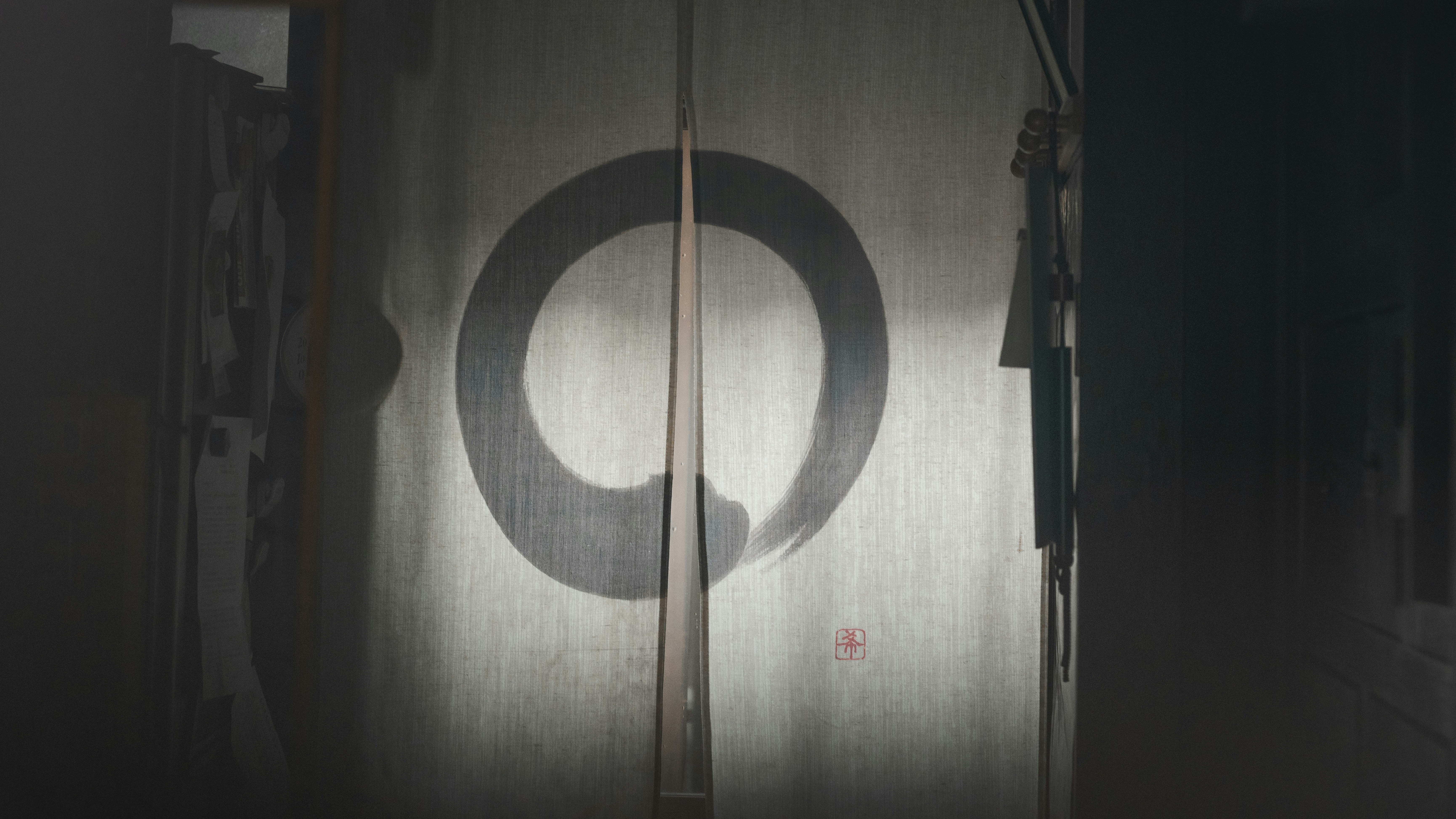 Enter a world of Zen with this photo of a white noren featuring a bluish ensō symbol. The ensō symbol, drawn in one continuous stroke, represents enlightenment and infinite potential. Against the pristine white fabric, the ensō is a minimalist yet striking contrast. Let this photo inspire stillness and clarity in your own life.