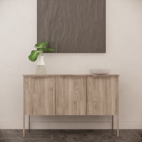A minimalist interior featuring a wooden sideboard with a light wood finish, adorned with a vase containing green leaves and a simple bowl. Above, a textured, gray artwork hangs on a textured white wall, contributing to the serene and modern feel of the space.