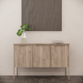 A minimalist interior featuring a wooden sideboard with a light wood finish, adorned with a vase containing green leaves and a simple bowl. Above, a textured, gray artwork hangs on a textured white wall, contributing to the serene and modern feel of the space.