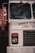 The front end of a vintage ice cream truck with visible headlight and black grille. The truck is painted white with blue text partially reading 'SOFT ICE CREAM.' Reflections and shadows indicate it is parked in an urban environment.