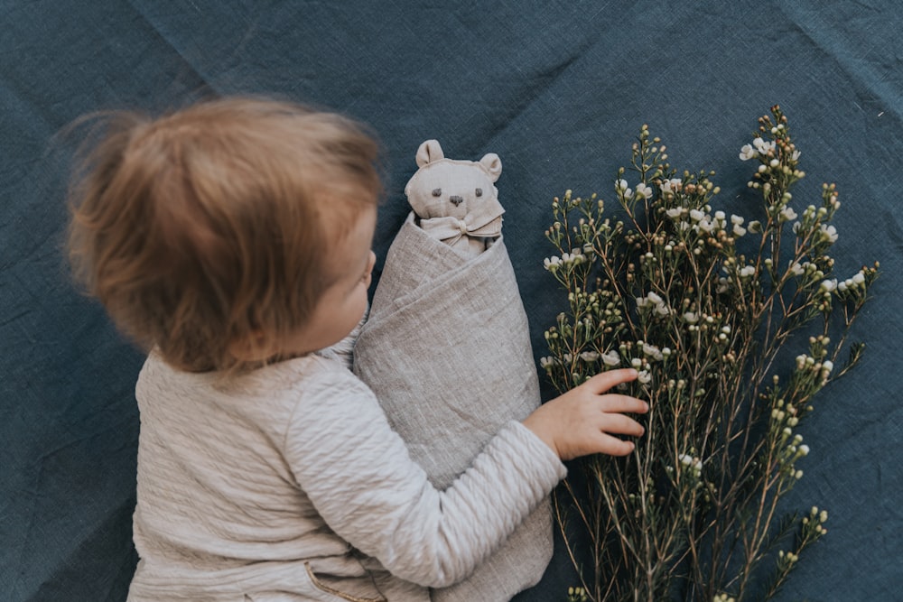 uma criança segurando um bicho de pelúcia ao lado de um ramo de flores