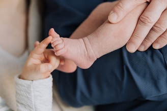 A close-up view of an adult gently holding a baby's foot while a child touches the baby's toes with delicate fingers, conveying a sense of tenderness and connection.