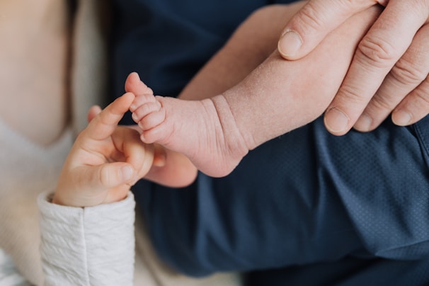 A close-up view of an adult gently holding a baby's foot while a child touches the baby's toes with delicate fingers, conveying a sense of tenderness and connection.