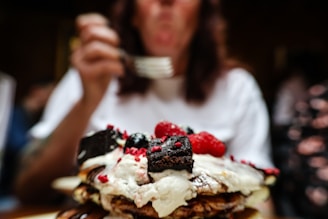 A close-up of a decadent waffle topped with fresh berries and whipped cream on a rustic wooden table.