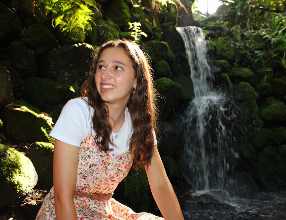 a young girl sitting in front of a waterfall