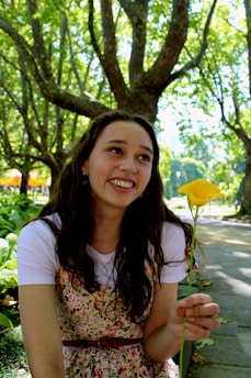 A cheerful young woman wearing a vintage floral dress smiling in a sunlit park