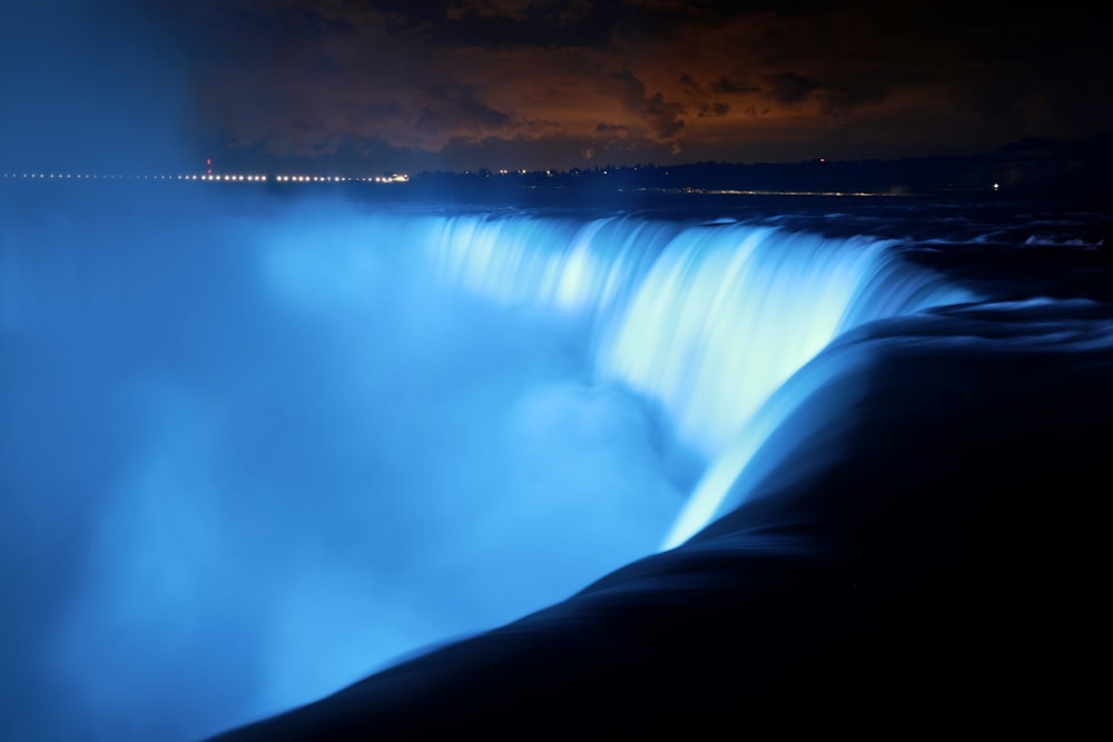 a large waterfall lit up at night with a sky background