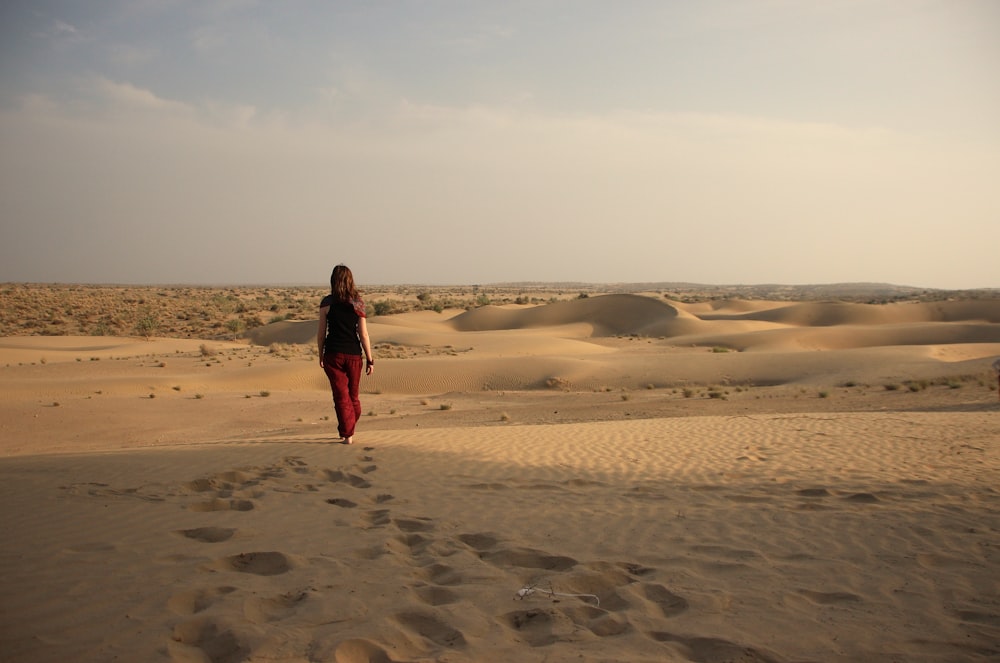a woman walking across a sandy field