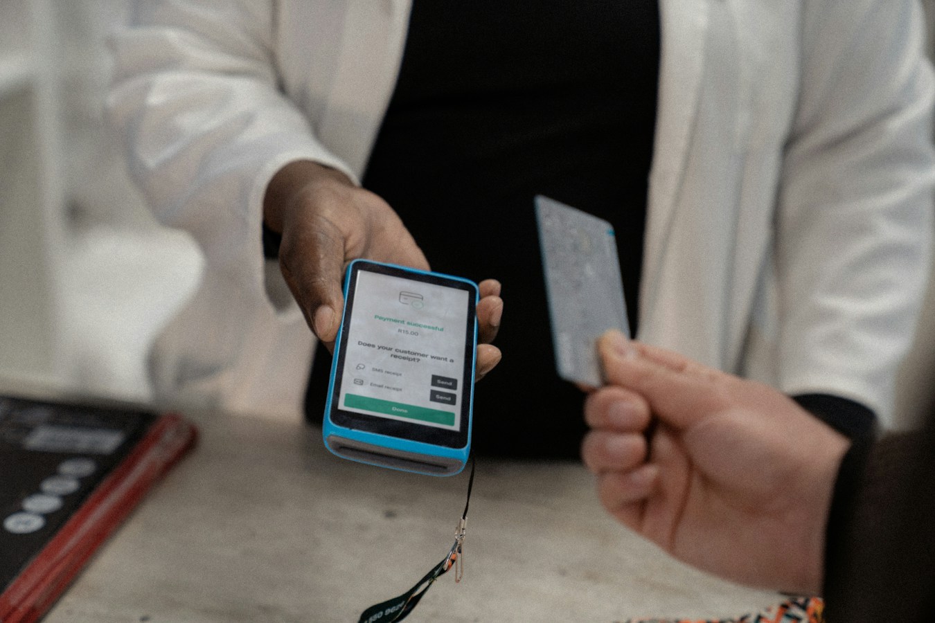 An African merchant in a white coat holds a small blue handheld payment terminal/phone showing a green 'Payment successful' screen while a customer's