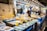 A bustling fish market with numerous stalls displaying a variety of fresh seafood on ice, including fish, shrimp, and other marine products. Each stall is equipped with bright signs indicating prices. Several vendors, wearing aprons and masks, are actively engaging with the produce and customers in a well-lit, busy environment.