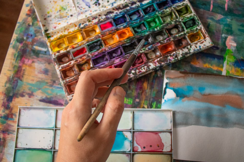 a person holding a paintbrush over a palette of paint