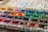 A well-used watercolor palette featuring a variety of vibrant colors, including shades of yellow, red, green, blue, and purple. The paints have been mixed and splattered across the palette, indicating frequent use. The surface of the palette is marked with paint splashes and stains, adding a textured and lively appearance.