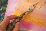 Close-up of hands mixing vibrant green and orange paints on a palette.