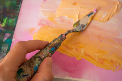 Close-up of hands mixing vibrant green and orange paints on a palette.