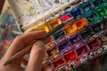 A cheerful artist’s hand holding a paintbrush over a canvas with fresh strokes of colour.