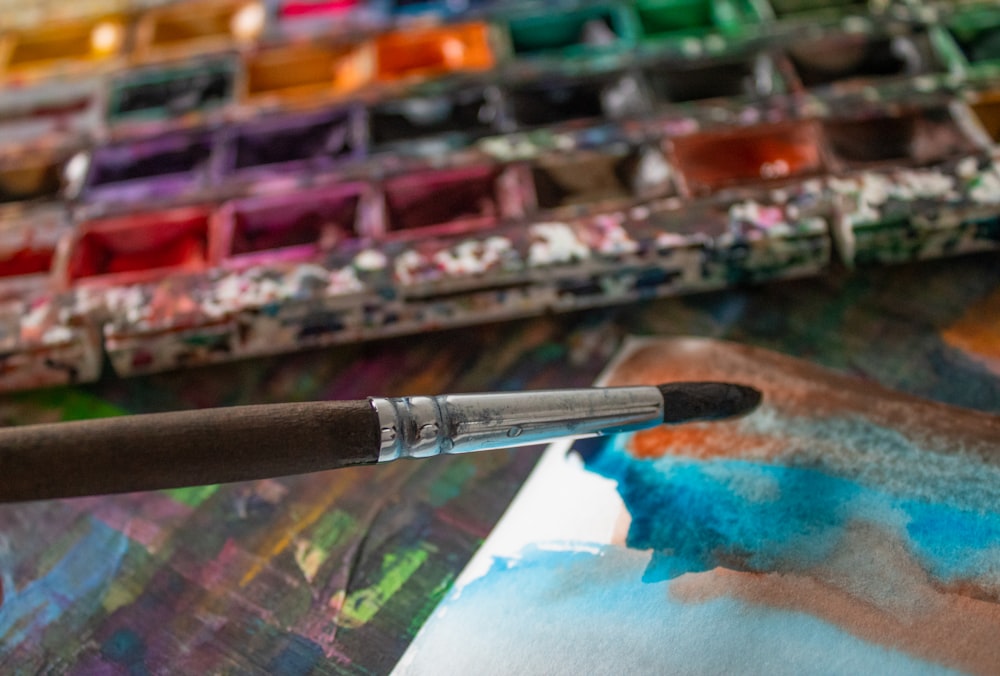 a close up of a paintbrush with a palette of paint in the background