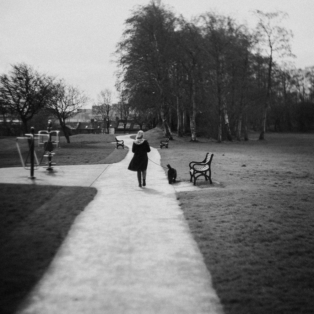 a woman walking down a sidewalk next to a park