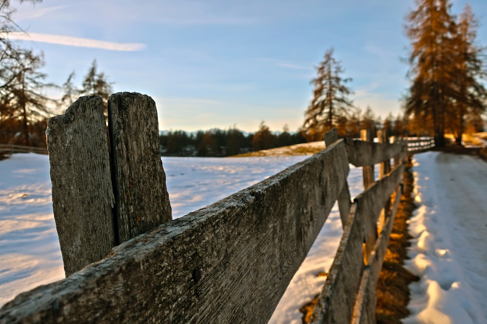 a wooden fence in the snow with trees in the background