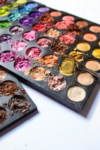 A close-up photo of a variety of colorful face powders arranged neatly on a wooden table.