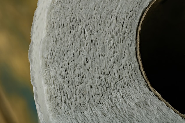 A detailed close-up of a toilet paper roll revealing the texture and layers of the paper wound around the cardboard tube. The focus is on the intricate pattern and structure of the paper, highlighted by soft lighting.