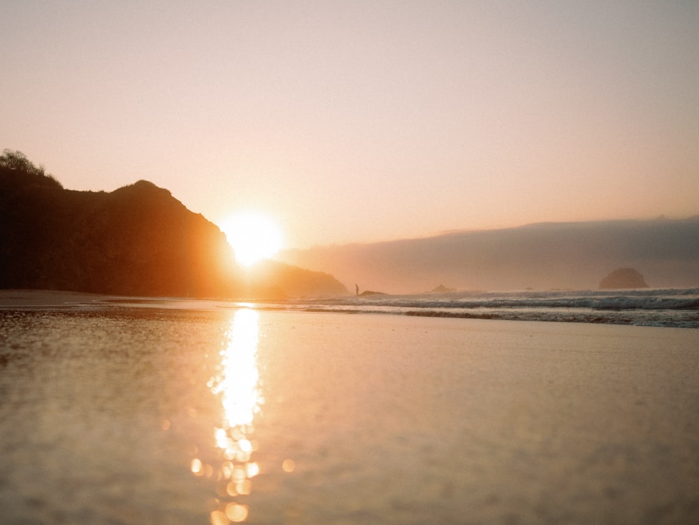 the sun is setting over the ocean on the beach