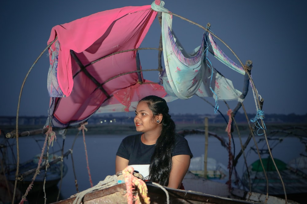 a woman sitting in a boat with a pink umbrella