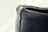 A close-up view of a textured, dark-colored leather edge with visible stitching. The surface appears slightly worn and rugged, with some frayed edges on the top side.